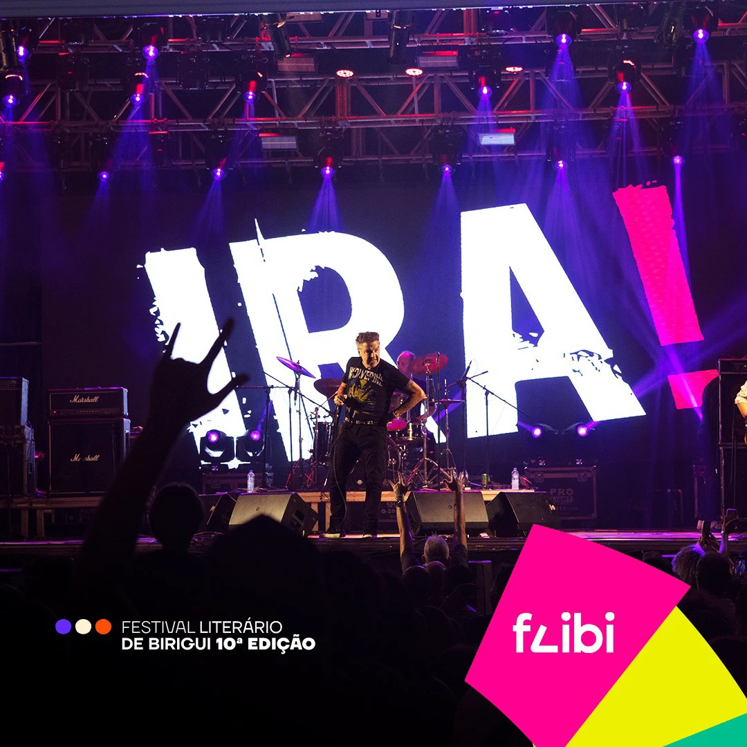 Show da banda IRA! no palco do festival, com o vocalista diante do telão com o nome da banda e o público de mãos erguidas.